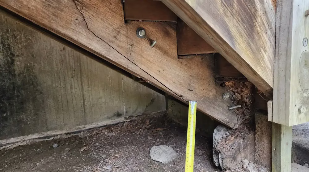 Close-up of a cracked and rotted stair stringer showing structural damage at the base, indicating the need for staircase remodeling